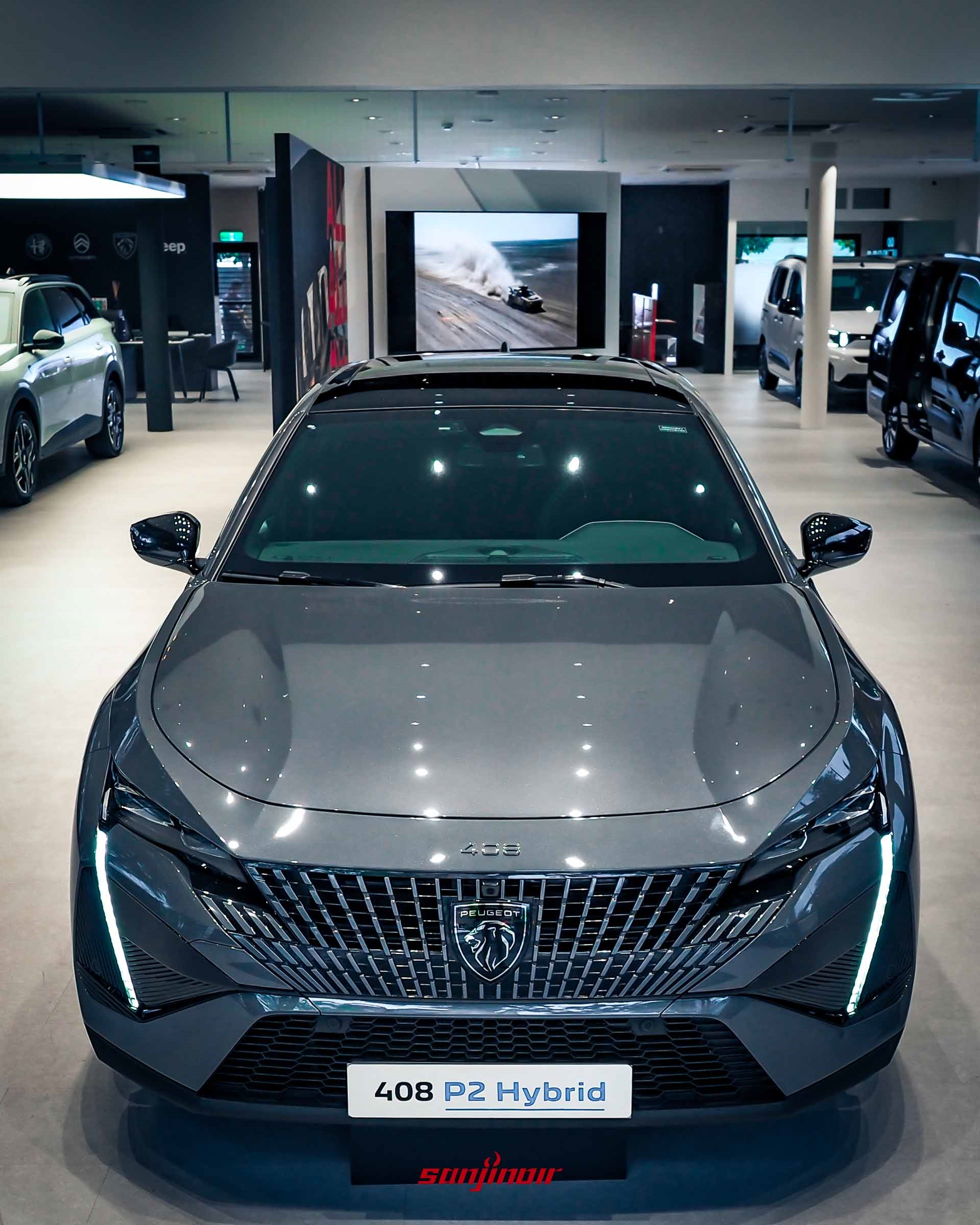 一輛灰色 PEUGEOT 408 P2 Hybrid 車頭特寫。車輛具有標誌性的垂直 LED 淚眼日行燈，巨大的車頭格柵中央是新款「Peugeot」獅子標誌。