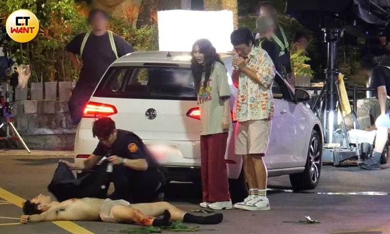 女主角曾莞婷穿著oversize的T恤搭配紅色寬鬆大睡褲現身,整體造型相當邋遢地與張啟樂一同看著躺在地上的鳳小岳。(圖/本刊攝影組)